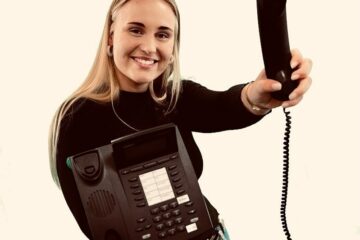 Eine junge, blonde Frau hält einen Telefonhörer