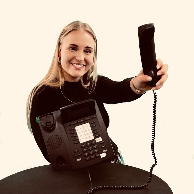 Eine junge, blonde Frau hält einen Telefonhörer
